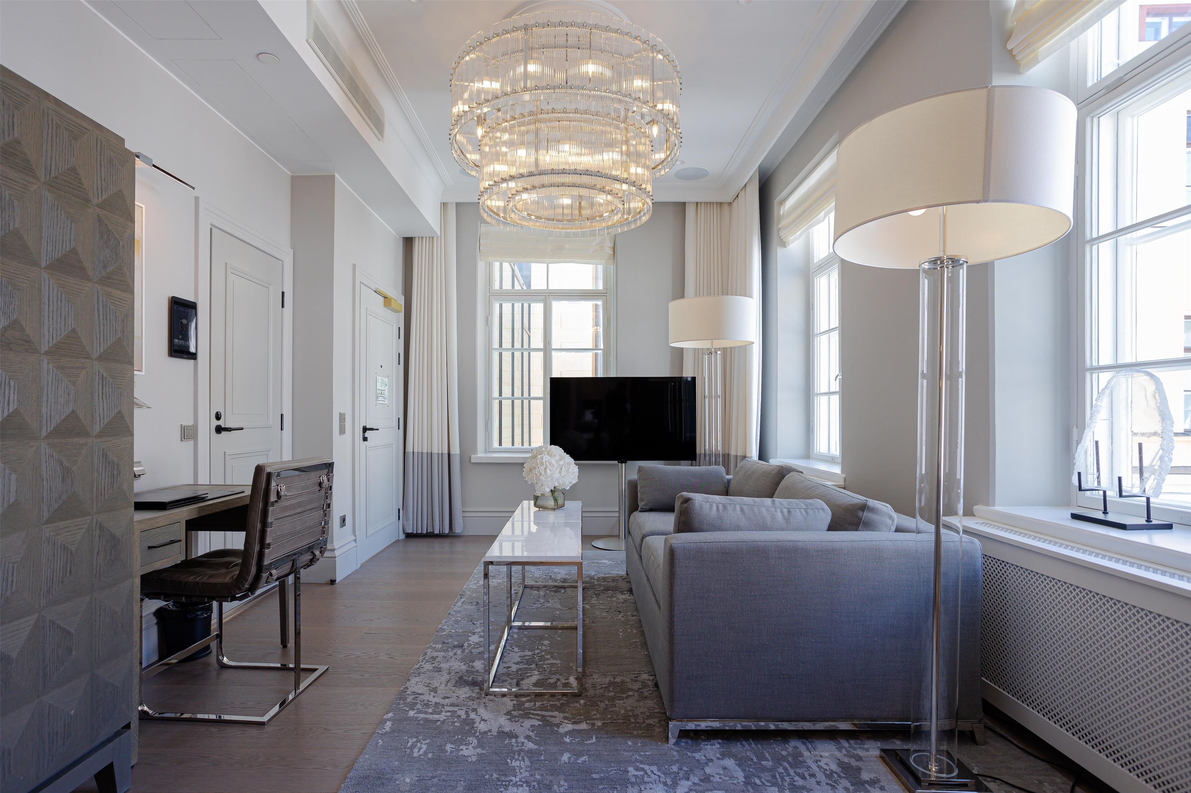 A modern living room with a chandelier, sofa, TV, and a desk with a chair.