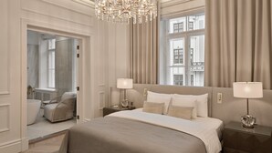 Ein Schlafzimmer mit einem großen Bett, zwei Nachttischen mit Lampen, einer Kandelaber und Blick auf Gebäude durch das Fenster.