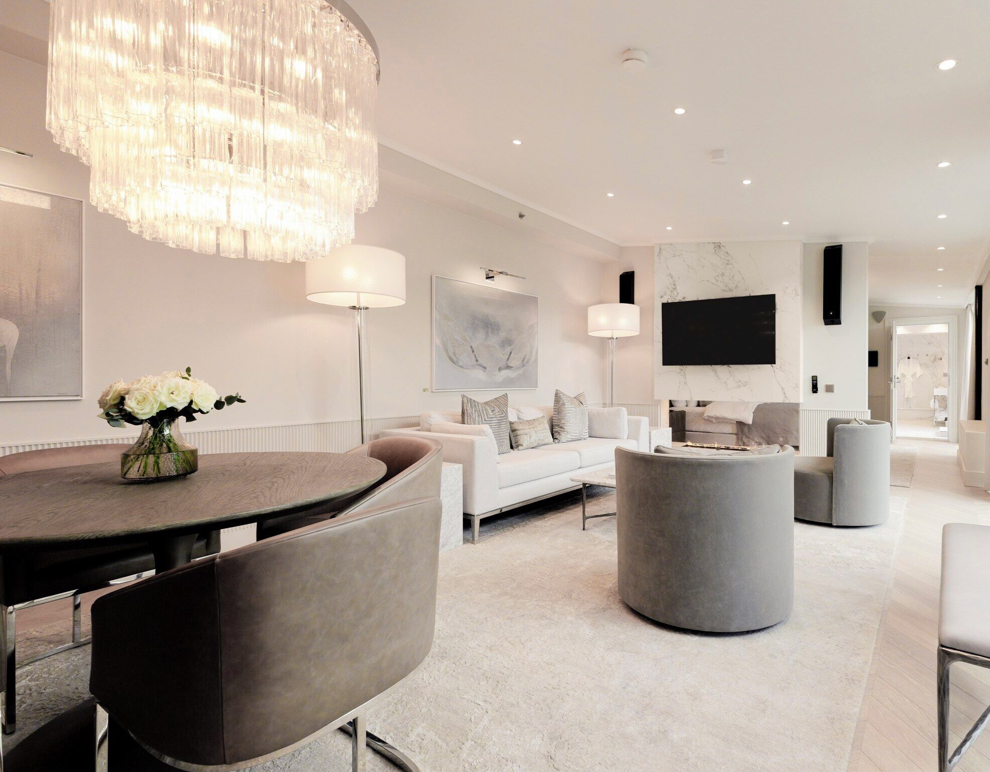A modern living room with a round dining table, grey sofas, and a large chandelier.