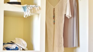 A storage unit with shelves containing folded clothes, a hat, and a basket with a yellow cloth. - Liogerma Studios (Kefalonia)