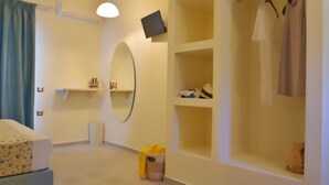 A hotel room with a bed, a mirror, a shelf with toiletries, a hanging robe, and a small basket. - Liogerma Studios (Kefalonia)