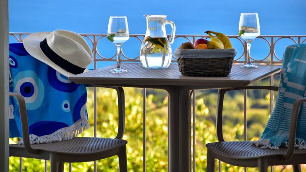 A table with a pitcher, glasses, a hat, and a fruit basket on a balcony with a view. - Liogerma Studios (Kefalonia)