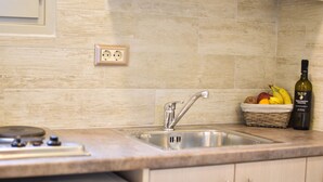 A kitchen with a sink, countertop, and a basket of fruit and a bottle. - Liogerma Studios (Kefalonia)
