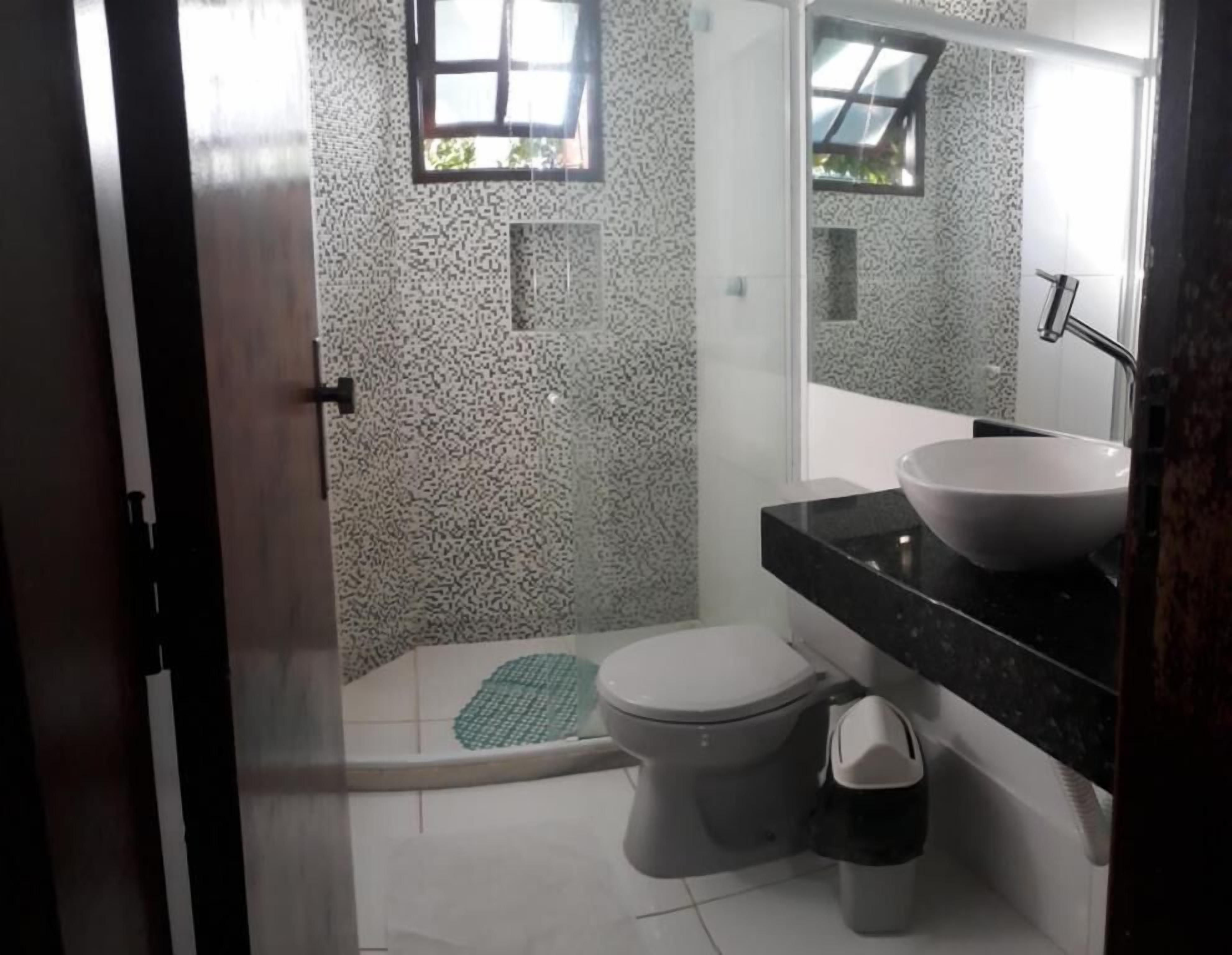 A bathroom with a white tiled floor, a white toilet, a black sink, and a mirror above the sink.