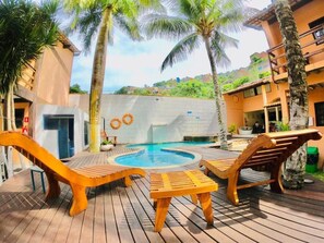 Una terraza de madera con piscina, sillas de descanso y palmeras.