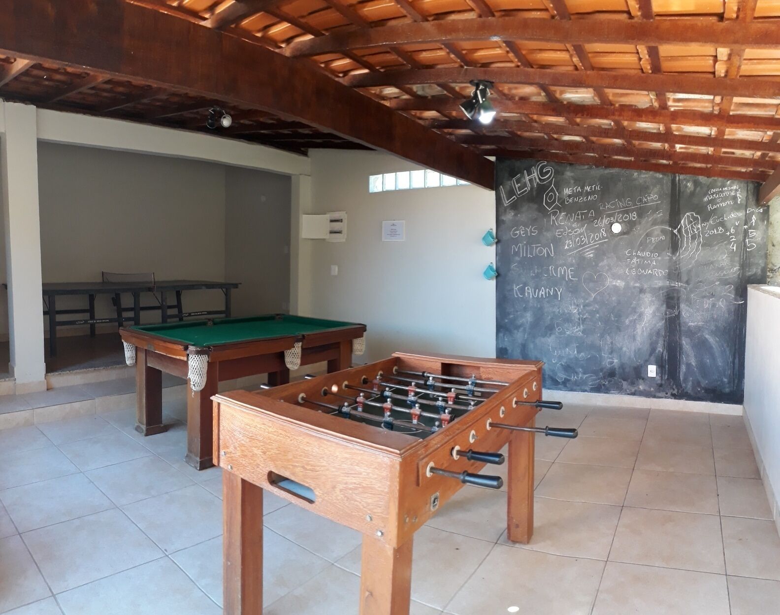 A room with a foosball table, a pool table, and a chalkboard with writing.