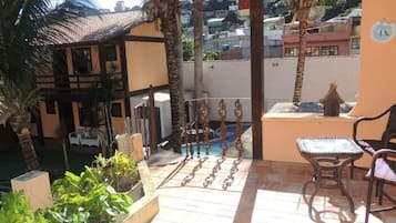 Un patio couvert avec une piscine, du mobilier d’extérieur et une vue sur le quartier environnant.