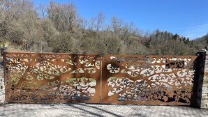 A metal gate with intricate leaf patterns, set against a backdrop of trees and a clear sky. - Quiet cottages (Prat-Bonrepaux)