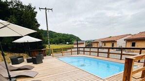 A wooden deck with a swimming pool, lounge chairs, and umbrellas. - Quiet cottages (Prat-Bonrepaux)