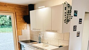 A modern kitchen with a central island, white cabinetry, and a black countertop. There are four white chairs with wooden legs around the island. - Quiet cottages (Prat-Bonrepaux)