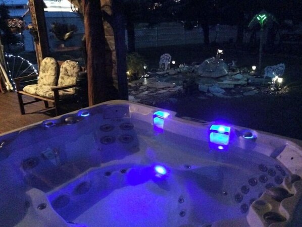 A hot tub with illuminated blue lights, surrounded by a stone patio and a chair.
