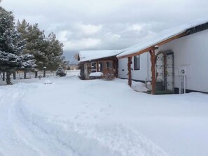 A snow-covered landscape with a wooden cabin and a white building with a covered porch.