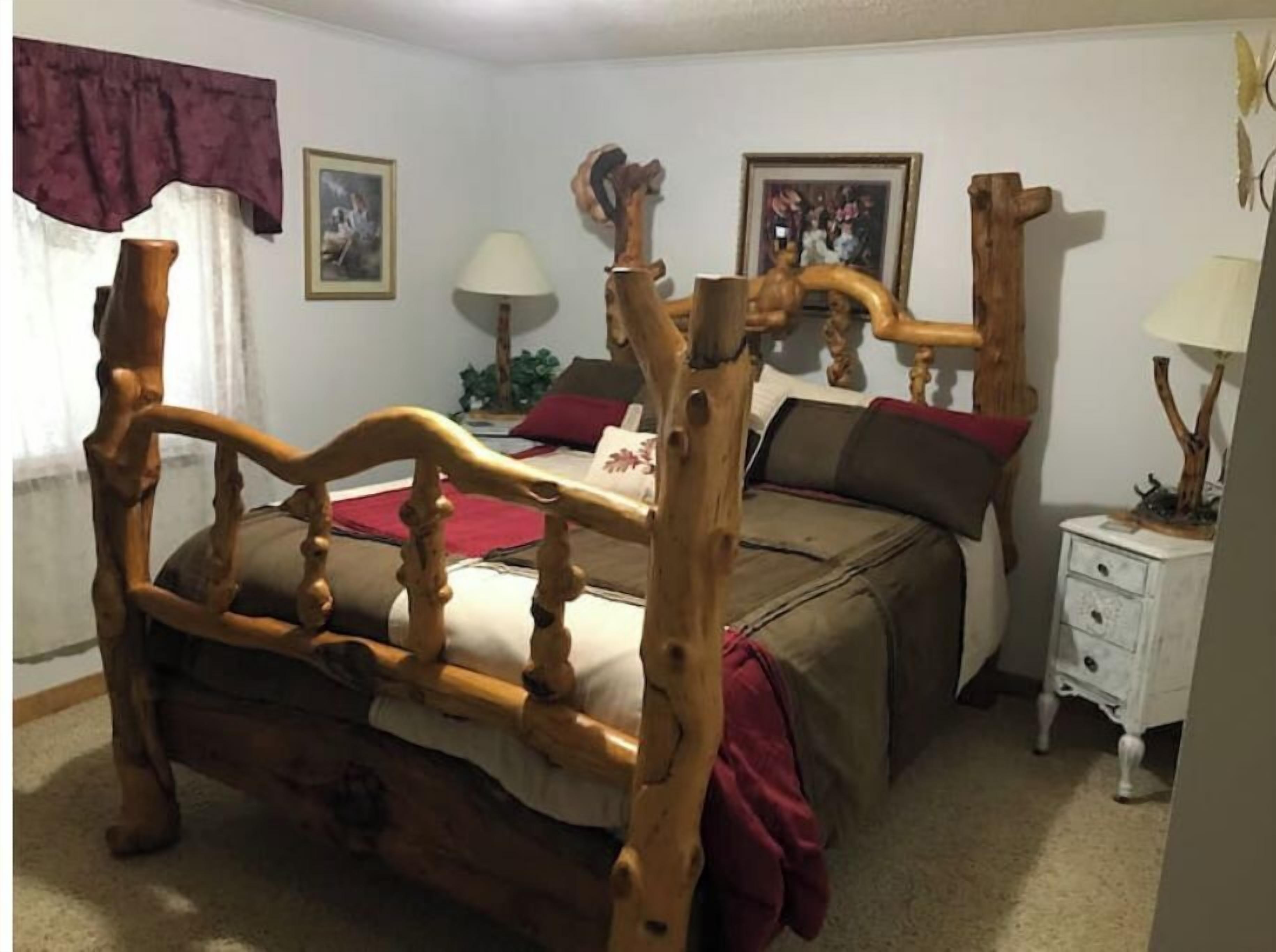 A bedroom with a wooden bed, a nightstand, a lamp, and a window with curtains.