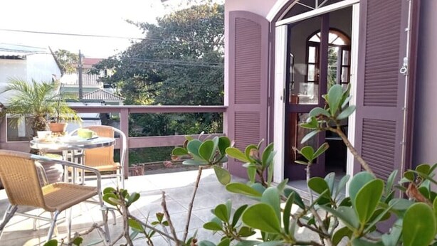 Un balcone con tavolo e sedie, una pianta in vaso e un edificio viola con persiane.