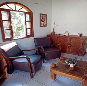 Quarto com duas poltronas de couro, uma mesa de centro de madeira e um aparador com objetos decorativos.