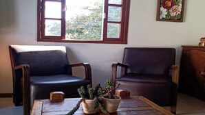 Una stanza con due poltrone scure, un tavolino in legno con piante in vaso, e un'ampia finestra ad arco che lascia entrare luce naturale.