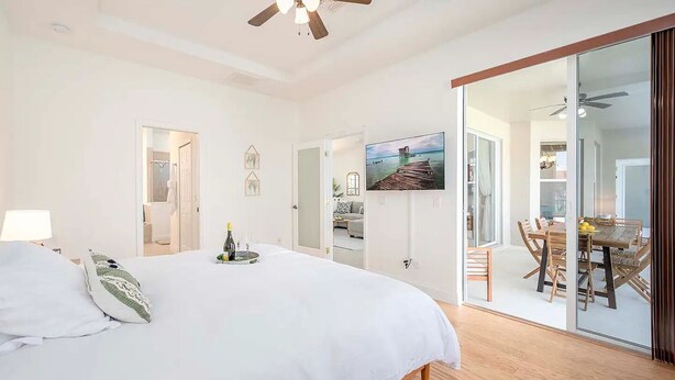A bedroom with a bed, a ceiling fan, a TV, and a dining area with a table and chairs.