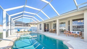 A swimming pool with a glass ceiling, surrounded by lounge chairs and a dining area.