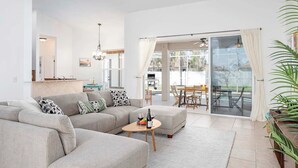 A modern living room with a grey sectional sofa, a small round coffee table, and a dining area with a glass door leading outside.