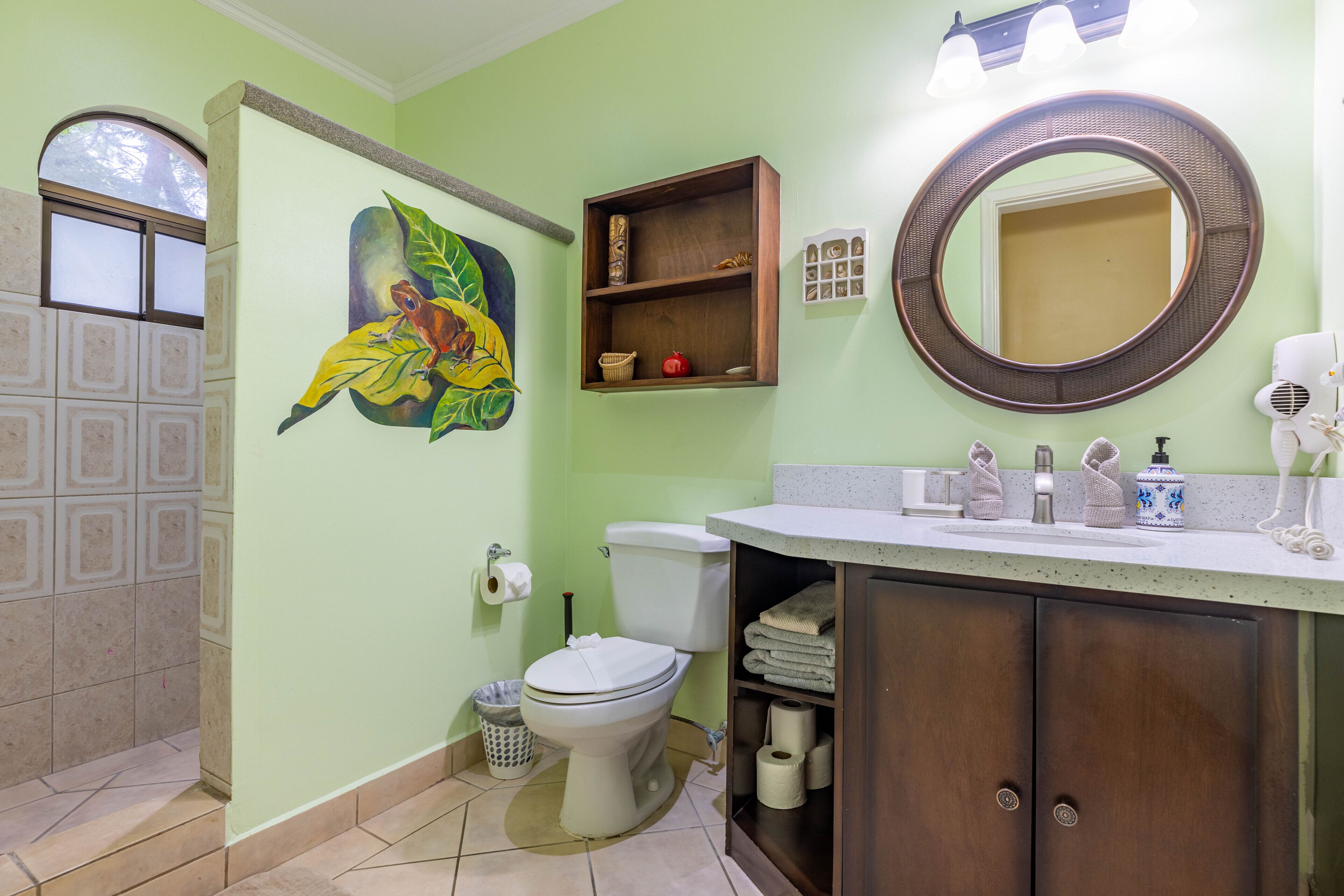 A bathroom with a toilet, sink, mirror, and a wall painting.