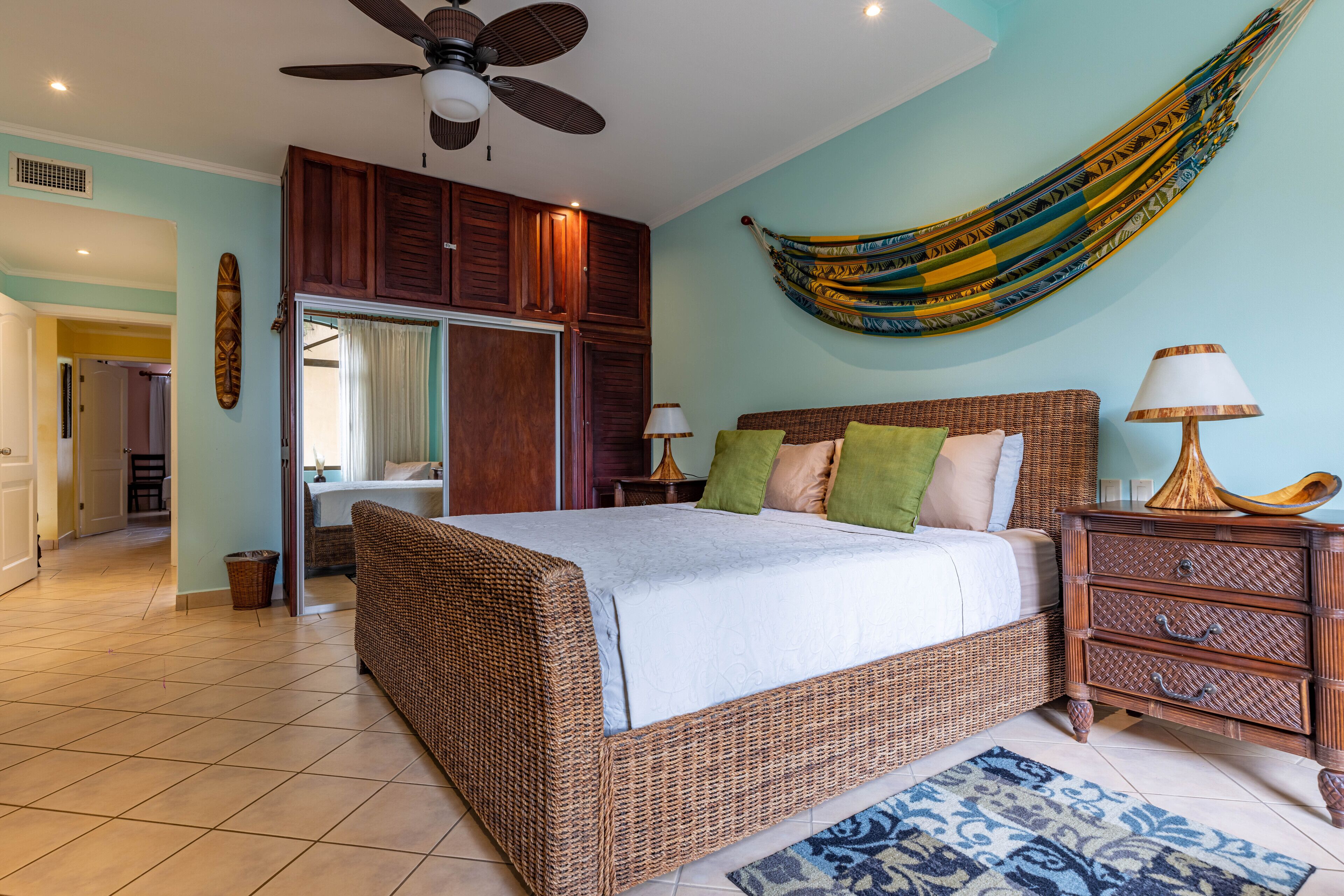 A spacious bedroom with a large bed, a ceiling fan, a hammock, and a nightstand with a lamp.