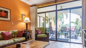 Ein Wohnzimmer mit einer Couch, einem Tisch und einem Sessel. Ein Fenster bietet Blick ins Freie.