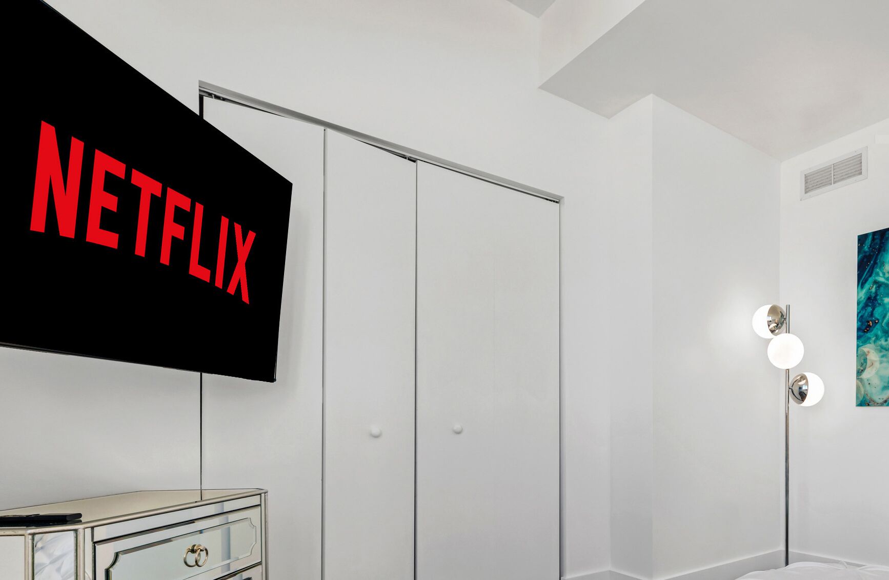 A modern bedroom with a wardrobe, a bedside table, and a wall-mounted TV displaying the Netflix logo.