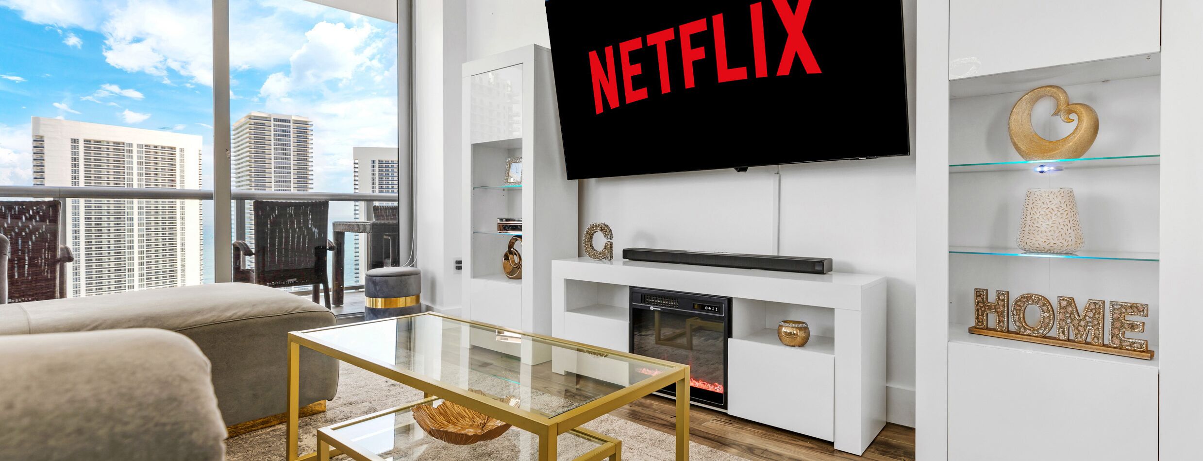 A modern living room with a large TV mounted on the wall, a fireplace, and a city view.