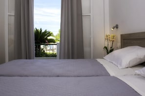 A hotel room with a bed, curtains, a nightstand, a lamp, and a view of a garden. - Yianetta Hotel (Corfu)