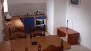 A compact kitchen with a built-in oven, a sink, and a small dining table with chairs.