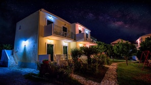 A two-story building with a balcony, a staircase, and a garden with flowers and a swing set. - Yianetta Hotel (Corfu)