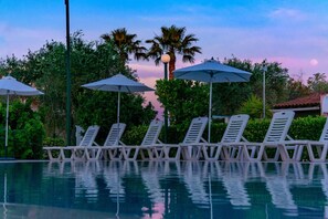 A pool area with lounge chairs and umbrellas, surrounded by greenery and palm trees. - Yianetta Hotel (Corfu)