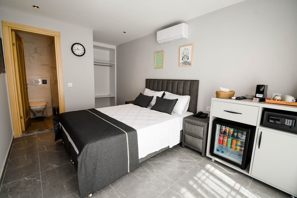 A modern hotel room with a bed, a small kitchenette, a toilet, and a wall-mounted clock.
