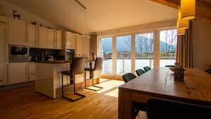 Una cocina moderna con armarios blancos, una mesa de comedor de madera y vistas a montañas a través de amplios ventanales.