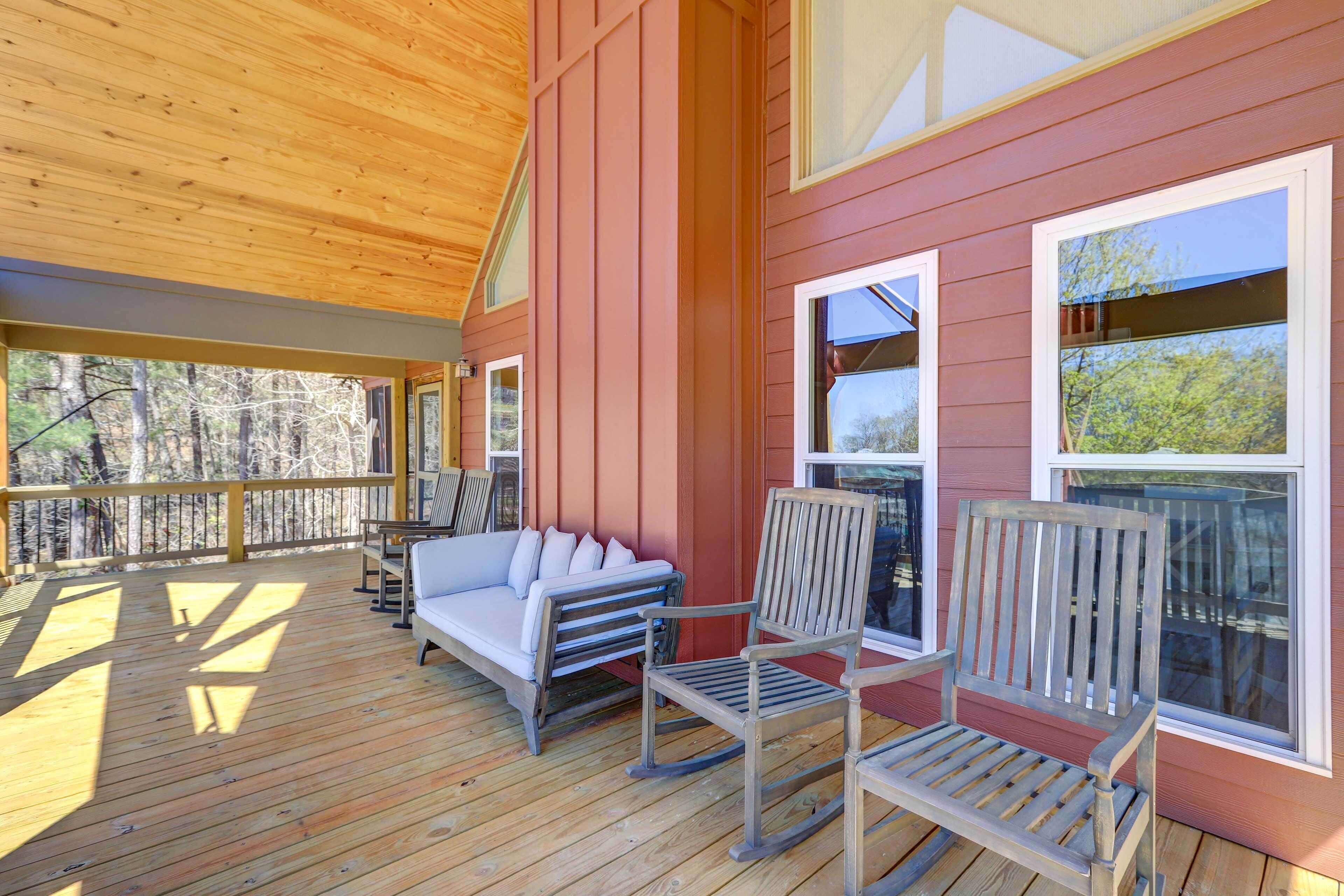 A wooden deck with a rocking chair and a sofa, large windows, and a view of trees.