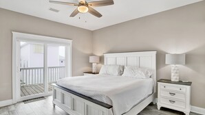 Una camera da letto con un letto, comodini, una ventola a soffitto e una porta vetrata scorrevole su un balcone.