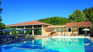 Una piscina con tumbonas y sombrillas, rodeada de edificios con tejados de tejas rojas.