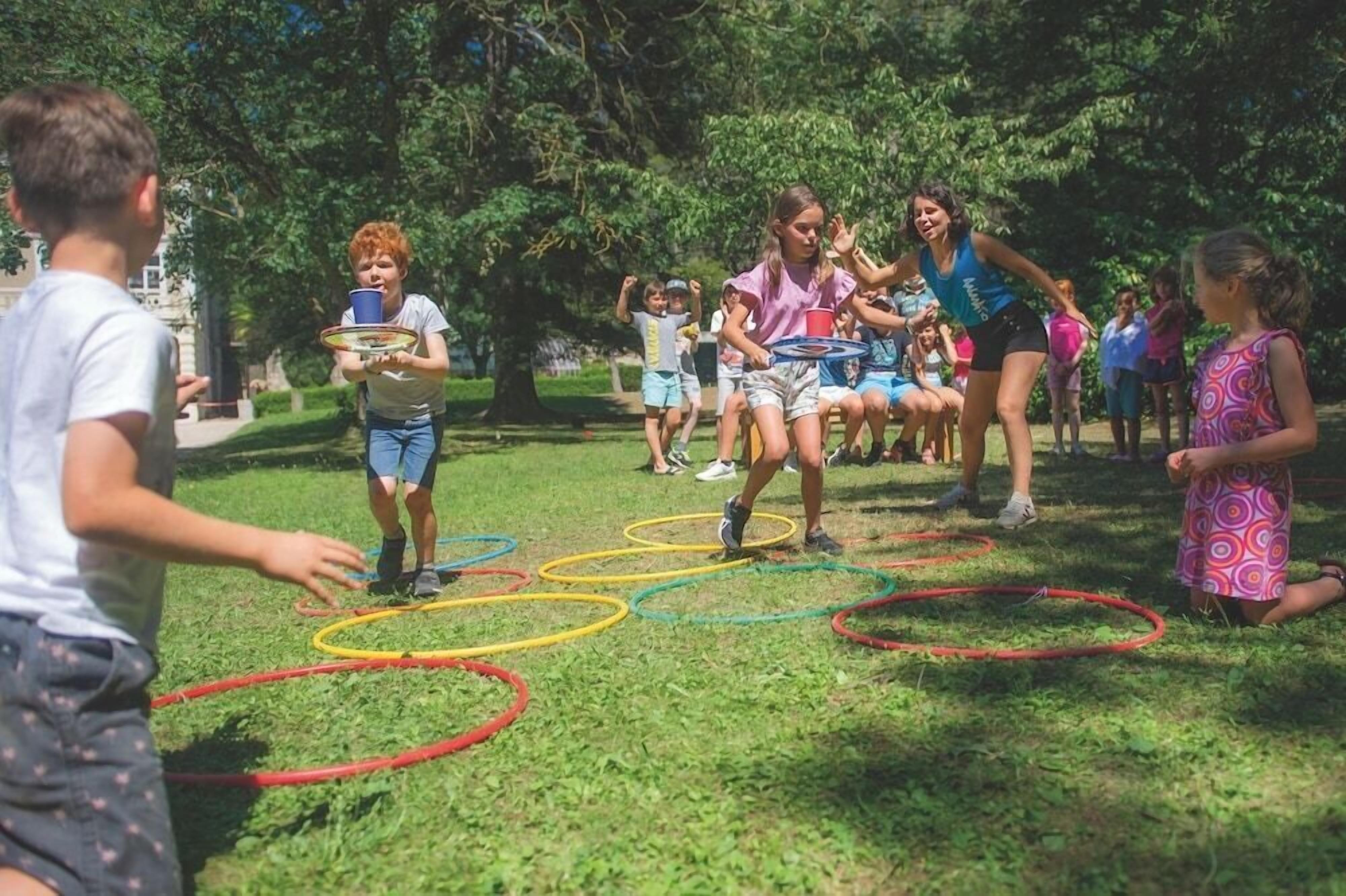 Eine Gruppe von Menschen spielt Hüpfspiel in einem Park mit Bäumen im Hintergrund.