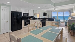 Une cuisine spacieuse avec un réfrigérateur noir, des armoires blanches et un coin repas comprenant une table et des chaises.