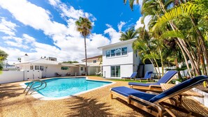 A swimming pool with lounge chairs, palm trees, and modern houses in the background. - The perfect Vacation next to the Ocean in the heart of Fort Lauderdale Beach. (Fort Lauderdale)