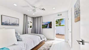 A modern bedroom with a bed, a ceiling fan, and a view of a beach through an open door. - The perfect Vacation next to the Ocean in the heart of Fort Lauderdale Beach. (Fort Lauderdale)