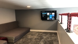 Una sala de estar con un sofá gris, una alfombra gris y un televisor de pantalla plana montado en la pared que muestra varios servicios de streaming.