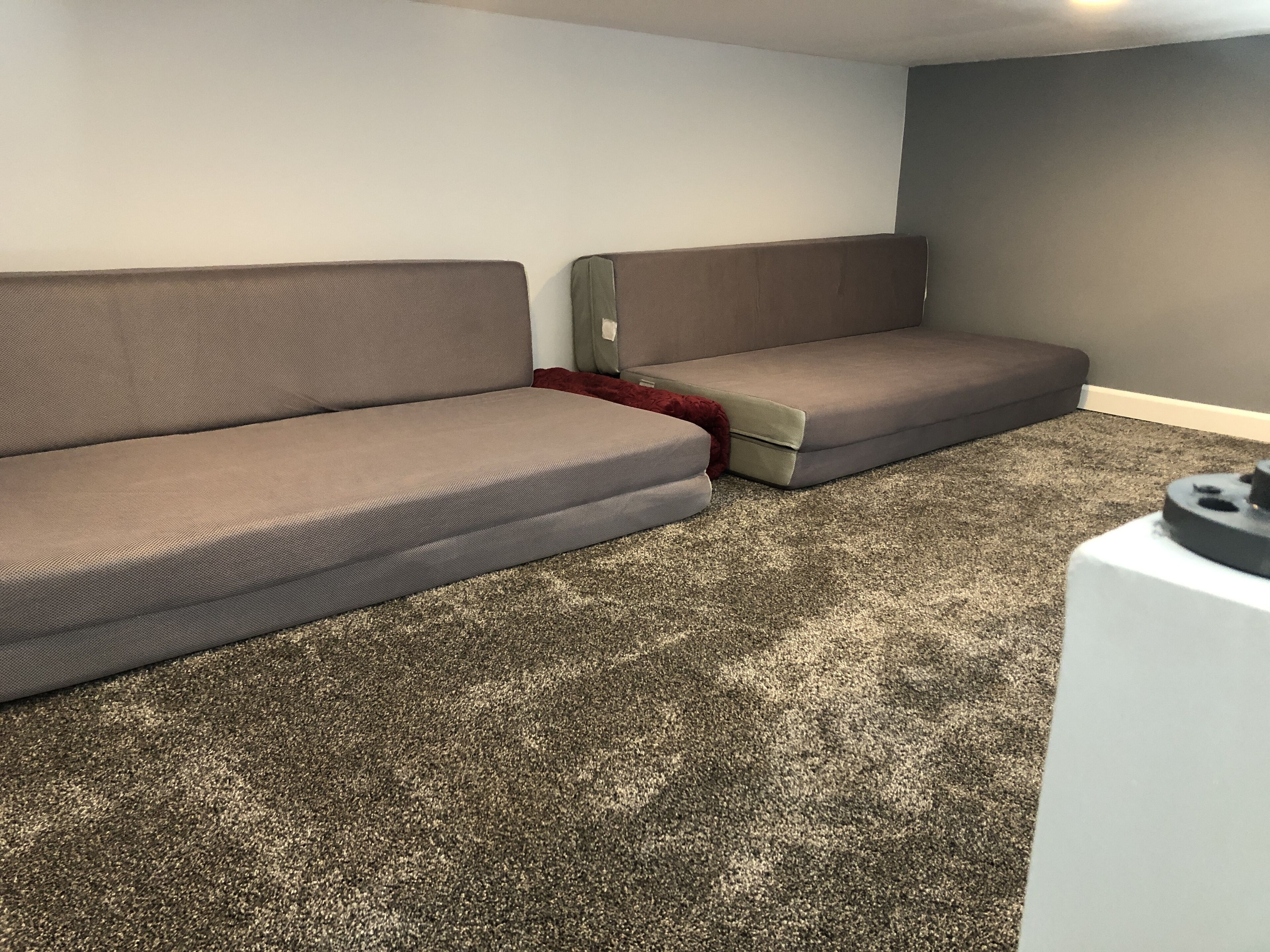 Une pièce avec deux canapés, un sol recouvert d’une moquette et une petite table sur laquelle se trouve un objet noir.