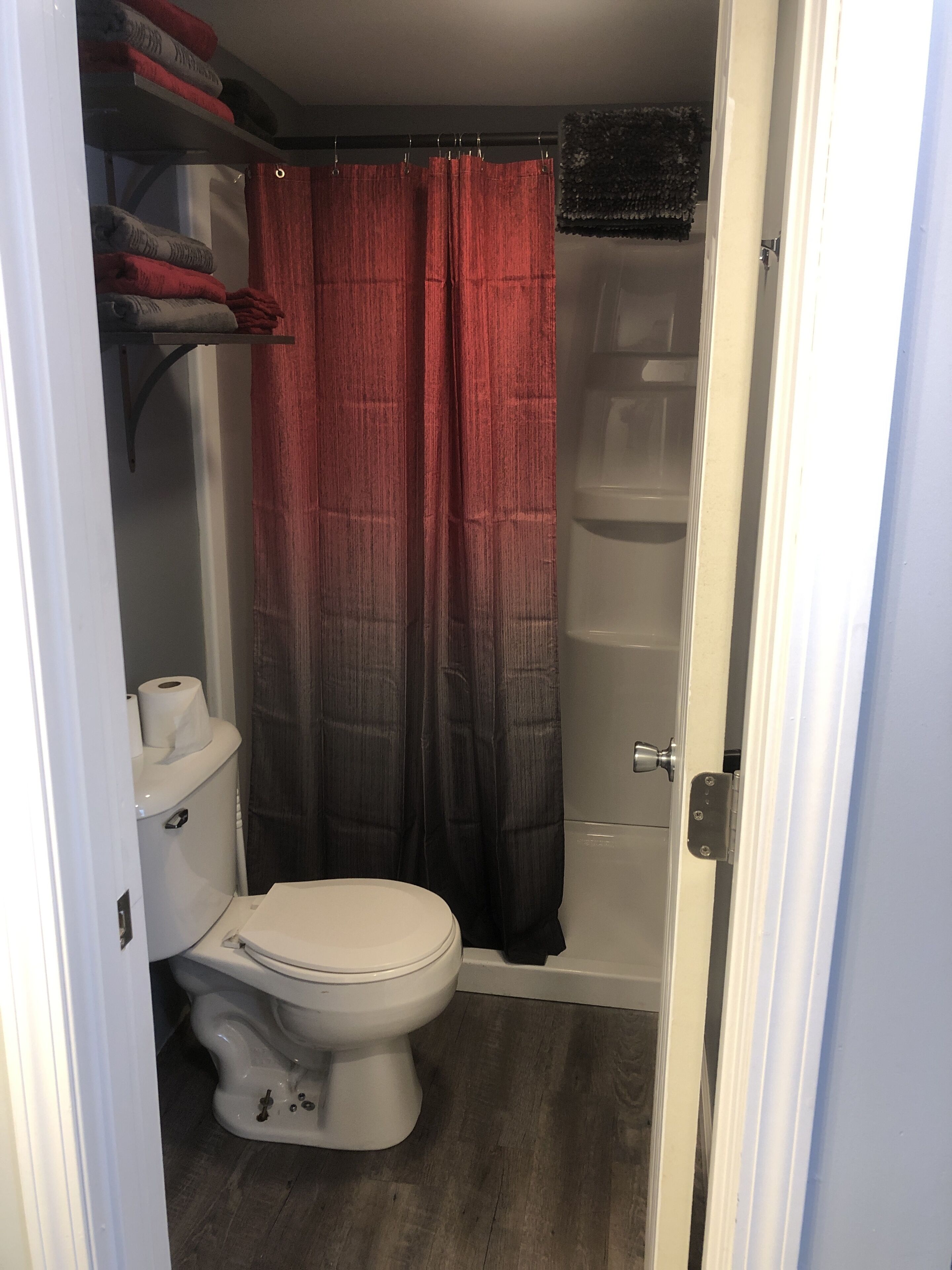 A bathroom with a toilet, a shower area, and a shelf with towels.