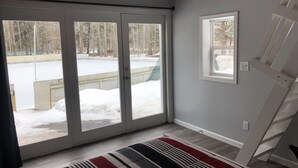 Una habitación con puerta de vidrio corrediza que da a un espacio exterior nevado, una ventana pequeña y una alfombra a rayas en el suelo.