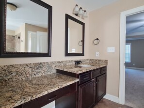 A bathroom with a granite countertop, a sink, dark cabinets, and two mirrors.