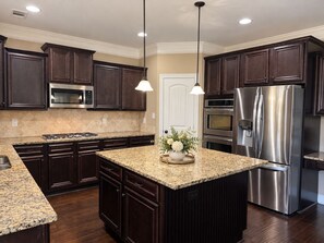 A modern kitchen with dark wood cabinets, stainless steel appliances, granite countertops, and pendant lighting.