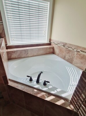 A bathroom with a freestanding bathtub, a window with blinds, and tiled walls.