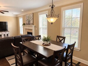 A dining area with a dark wooden table, six chairs, a central vase with greenery, and a wall-mounted light fixture.