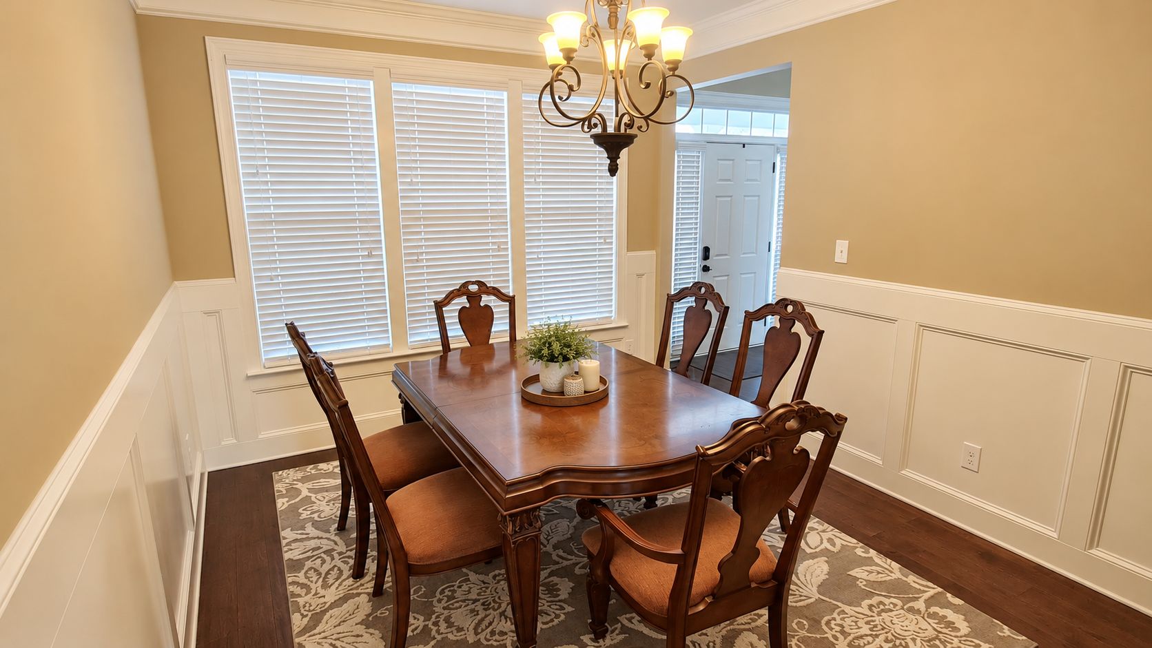A dining room with a wooden table and chairs, a chandelier, and a window with blinds.